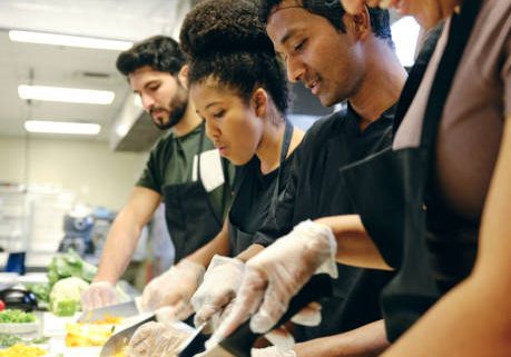 A teaching chef works with a group of students in a commercial kitchen.